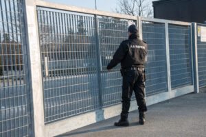 Una GPG è in piedi di fronte ad un cancello di una zona industriale voltata di schiena